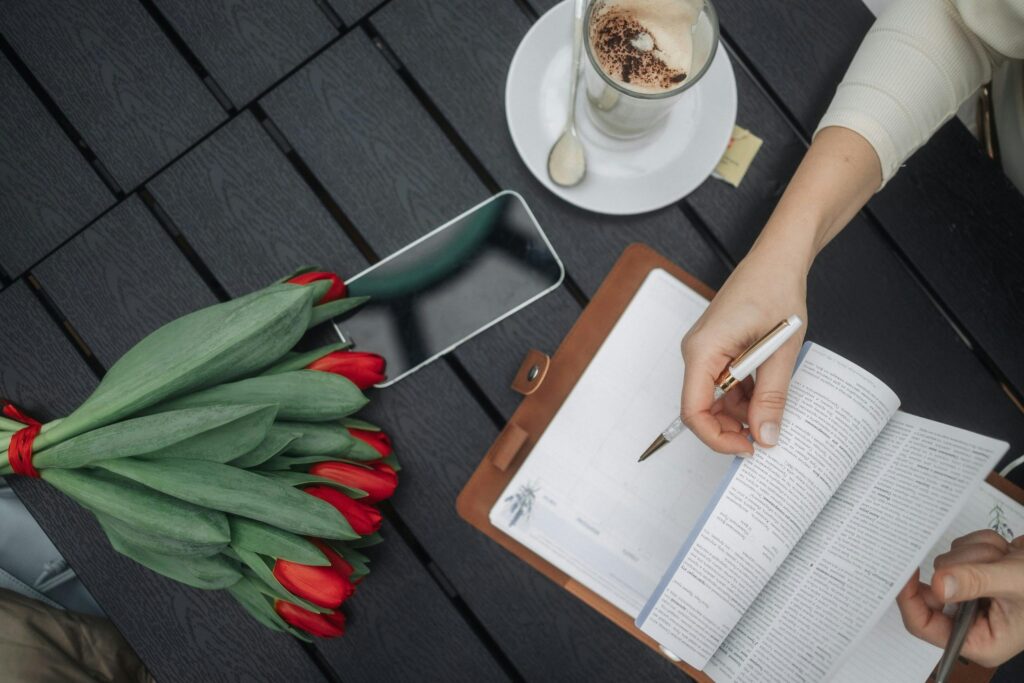 pexels-photo-30706230-30706230 A flat lay of an open planner, a bouquet of red tulips, and coffee on a dark table outdoors.